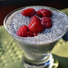 glass cup of chia pudding topped with raspberries on a green placemat
