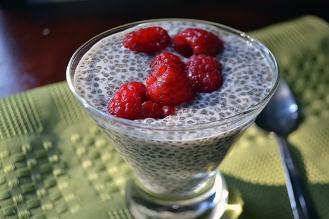 glass cup of chia pudding topped with raspberries on a green placemat 