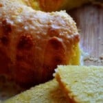 Slices of grapefruit poundcake in the foreground with a partial bundt cake in the background, set aganist a dark background with low lighting