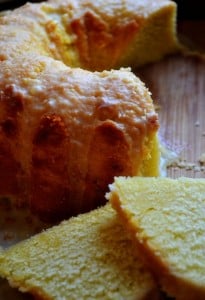 Slices of grapefruit poundcake in the foreground with a partial bundt cake in the background, set aganist a dark background with low lighting