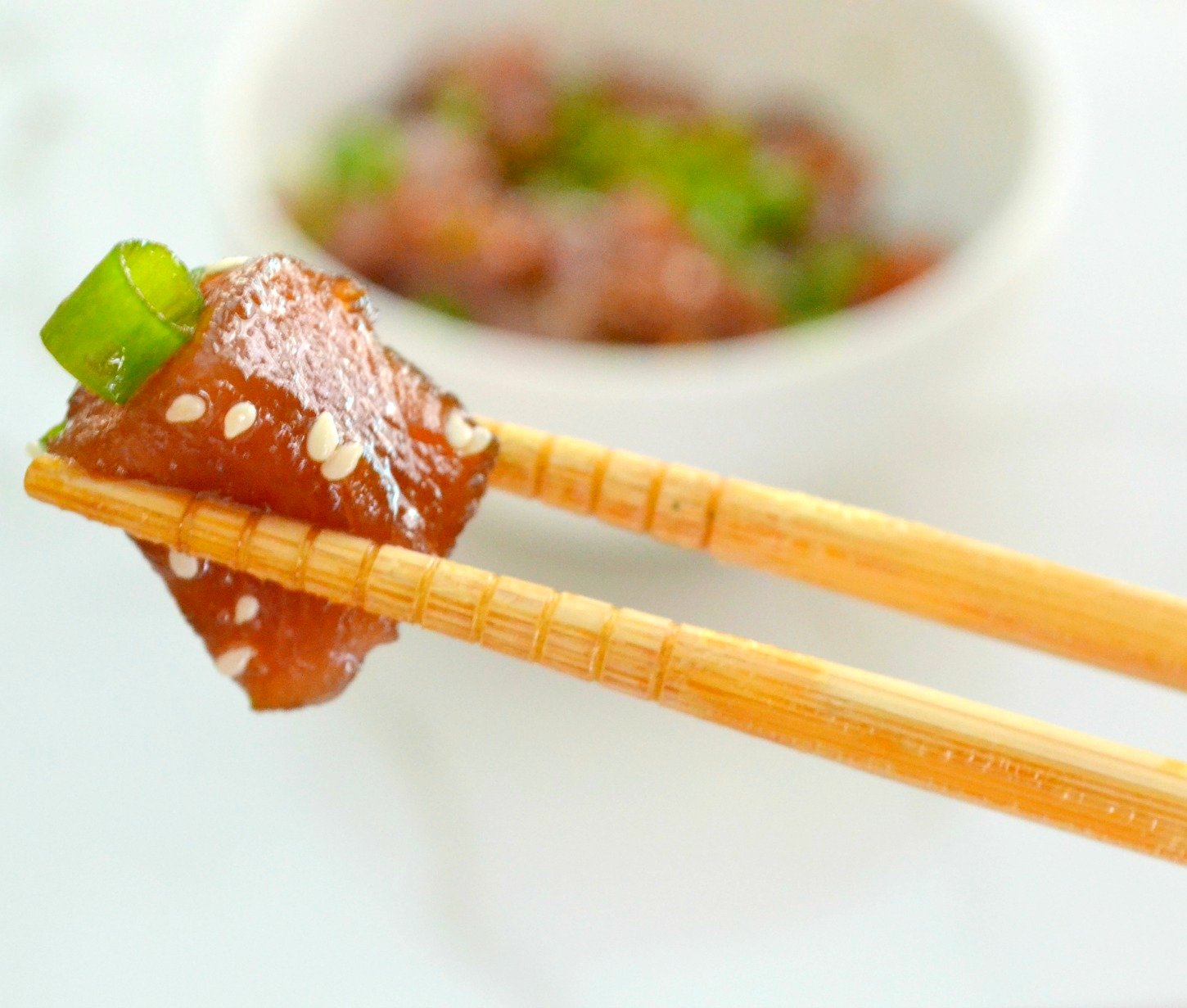 chunk of tuna poke between two chopsticks on a white background