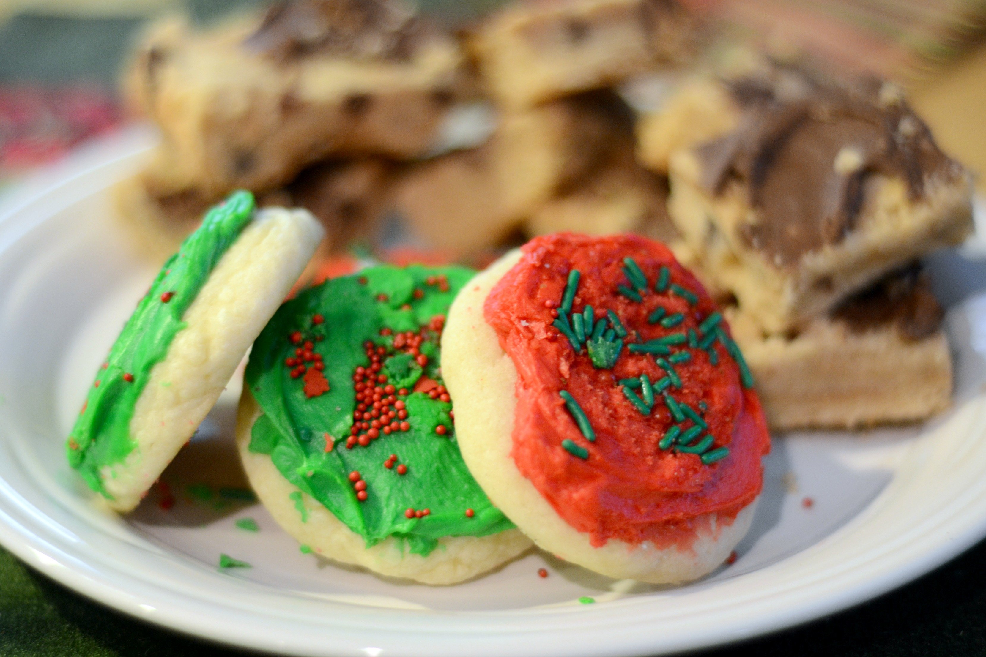 A plate of festive holiday cookies, featuring red and green soft sugar cookies with Christmas sprinkles. 
