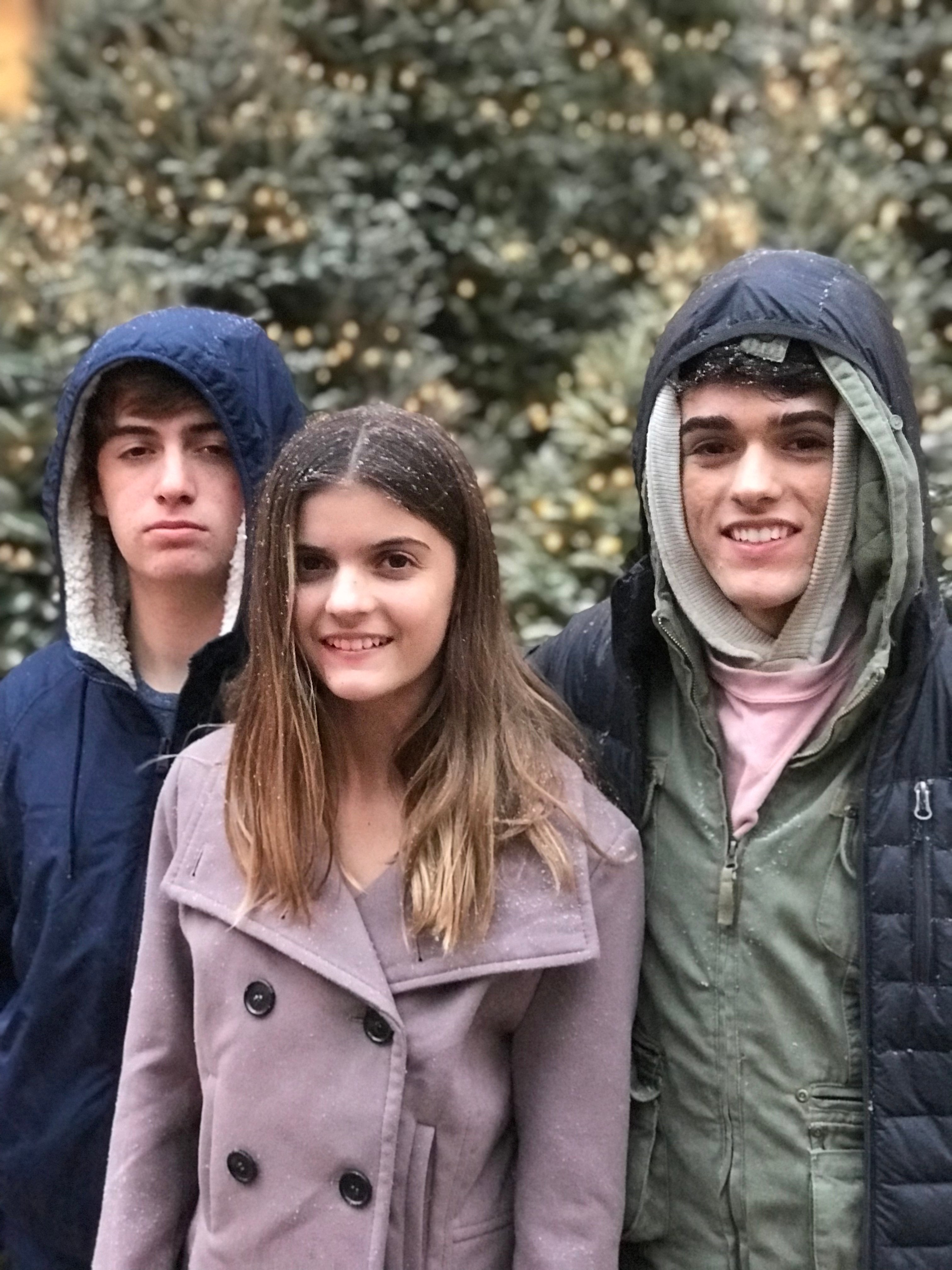three teens posing for a picture in front of lit Christmas trees new york city