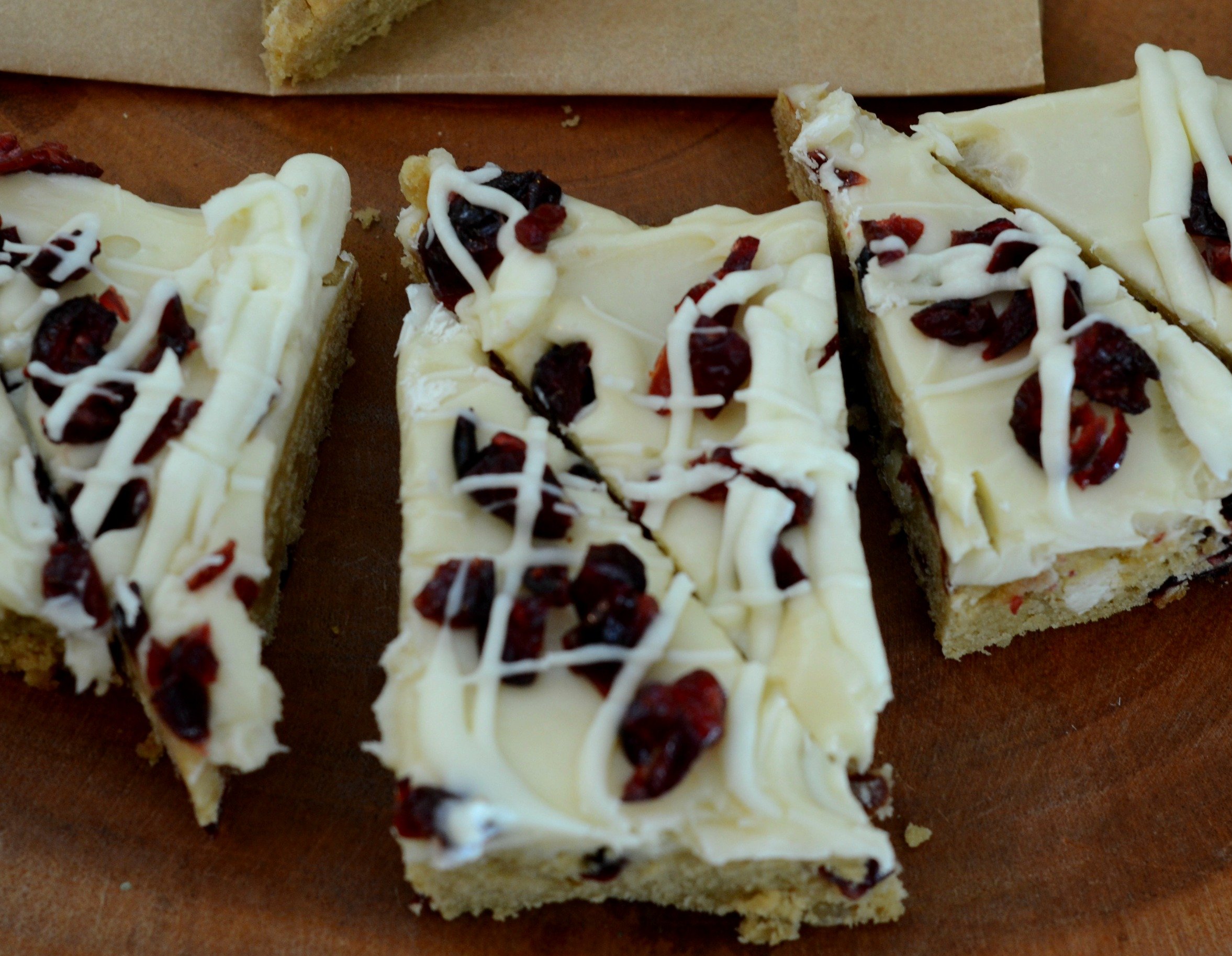 Overhead view of white chocolate blondies covered with cream cheese frosting, cranberries and a white drizzle. 