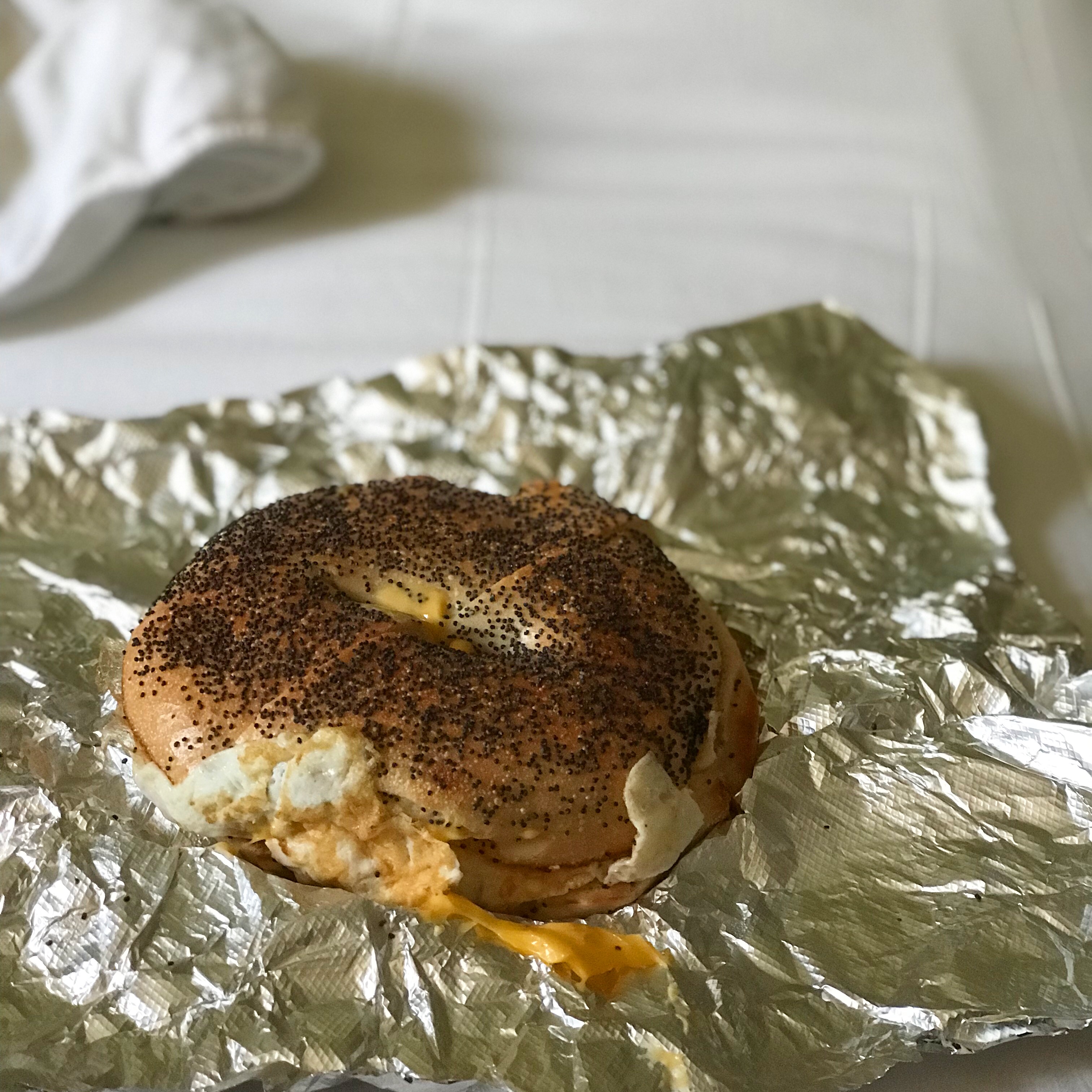 bagel egg and cheese on foil wrapper, sitting on hotel room bed
