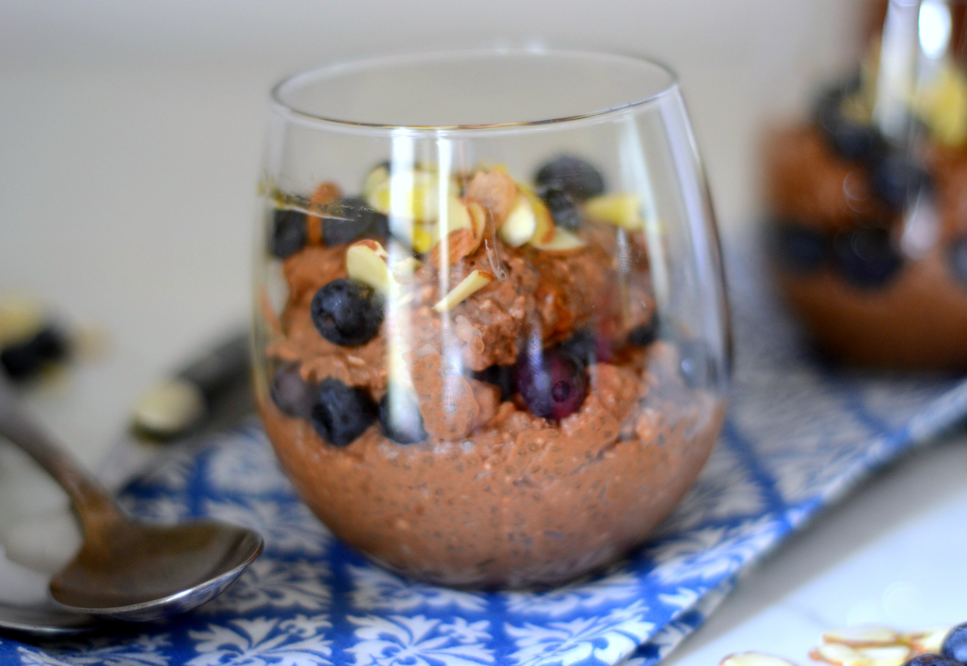 glass dish filled with chocolate chia pudding topped with slivered almonds and blueberries