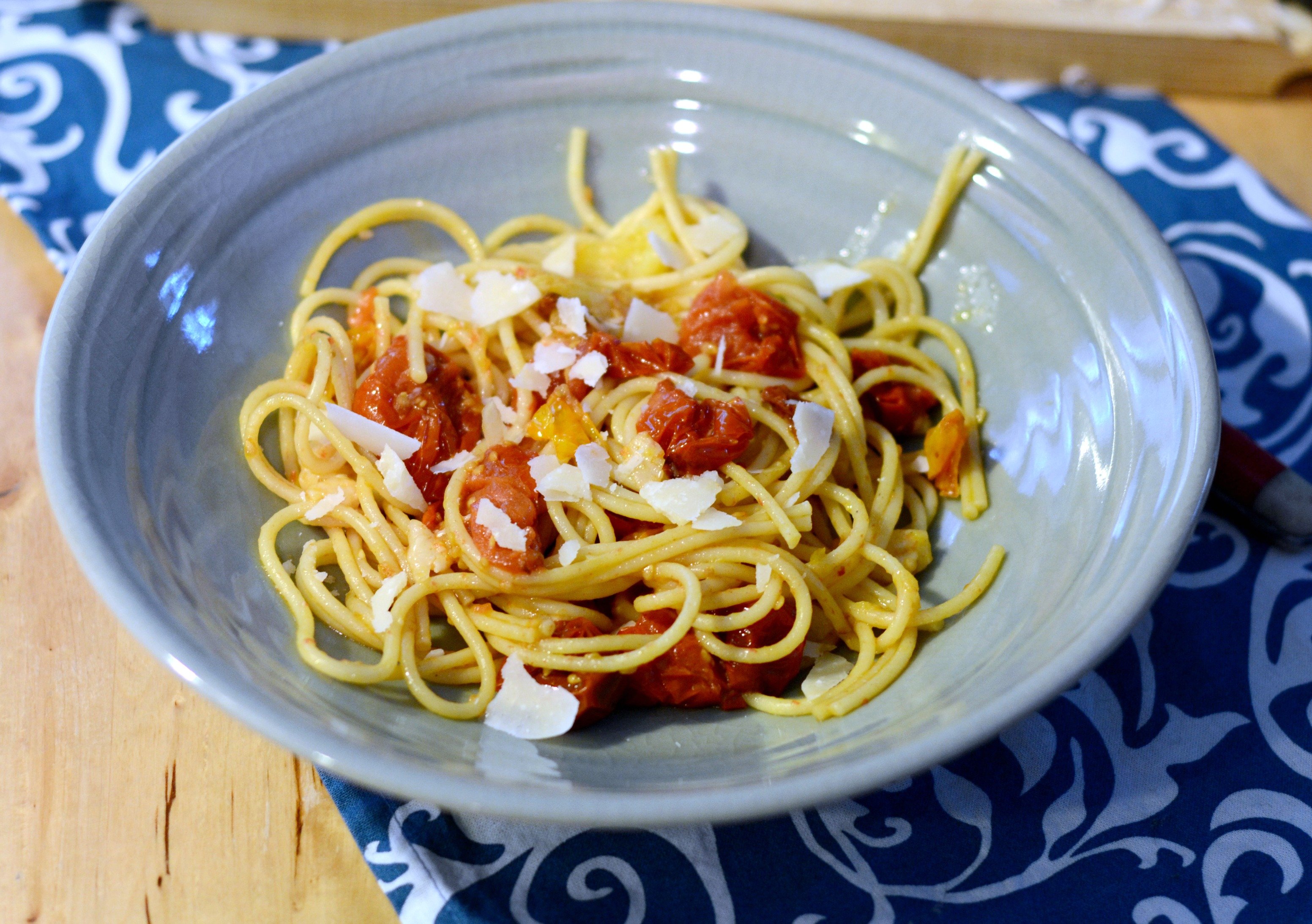 overhead view of a bowl of pasta sprinkled with roasted tomatoes and Parmesan cheese