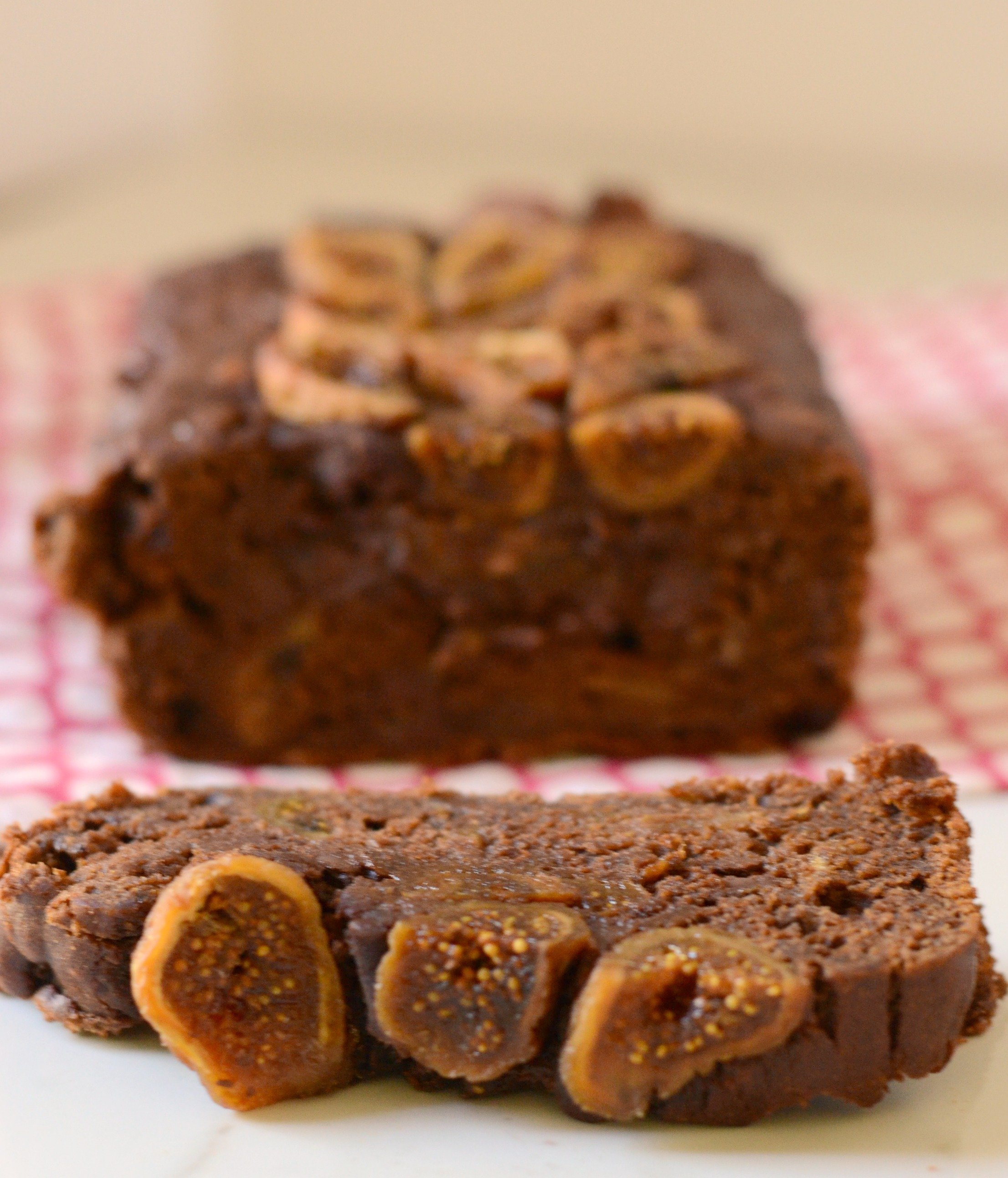 Slice of chocolate fig banana bread in the foreground with remaining loaf in the background