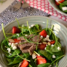 bowl of spinach and other greens topped with strawberries, steak and goat cheese