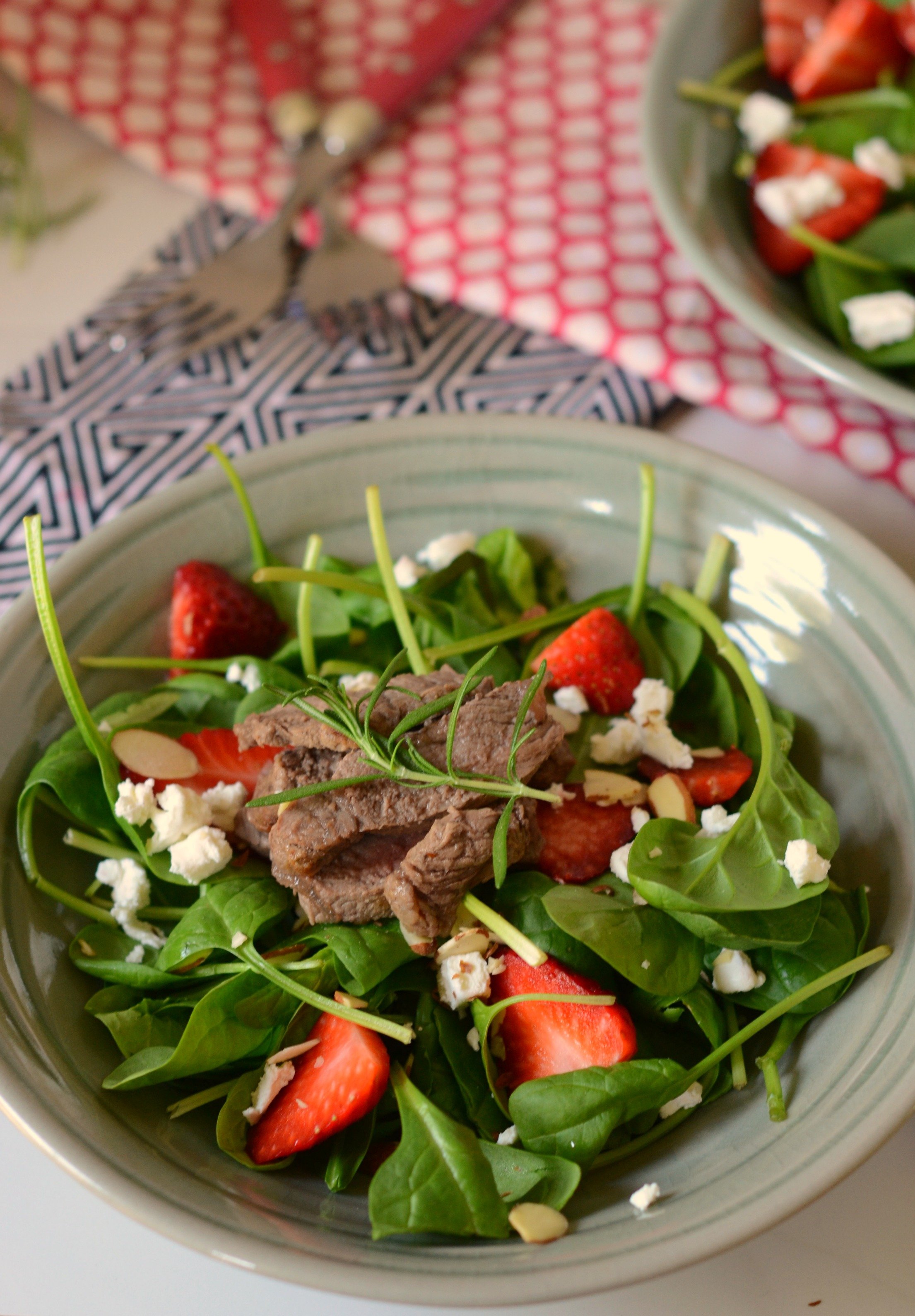 bowl of spinach and other greens topped with strawberries, steak and goat cheese