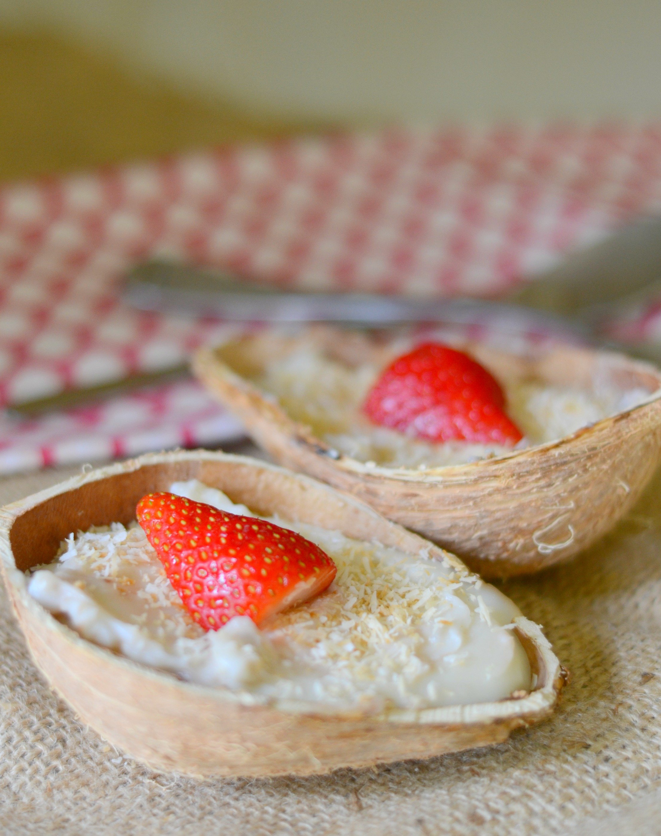 vegan coconut pudding in coconut shells topped with toasted coconut and strawberries