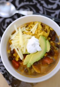 Overhead view of a bowl of vegetarian tortilla soup topped with sour cream, cheese and avocados