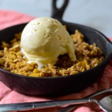 cast iron pan with peach crisp topped with vanilla ice cream