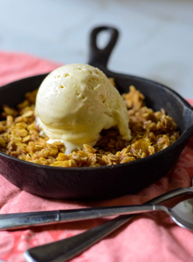 cast iron pan with peach crisp topped with vanilla ice cream 