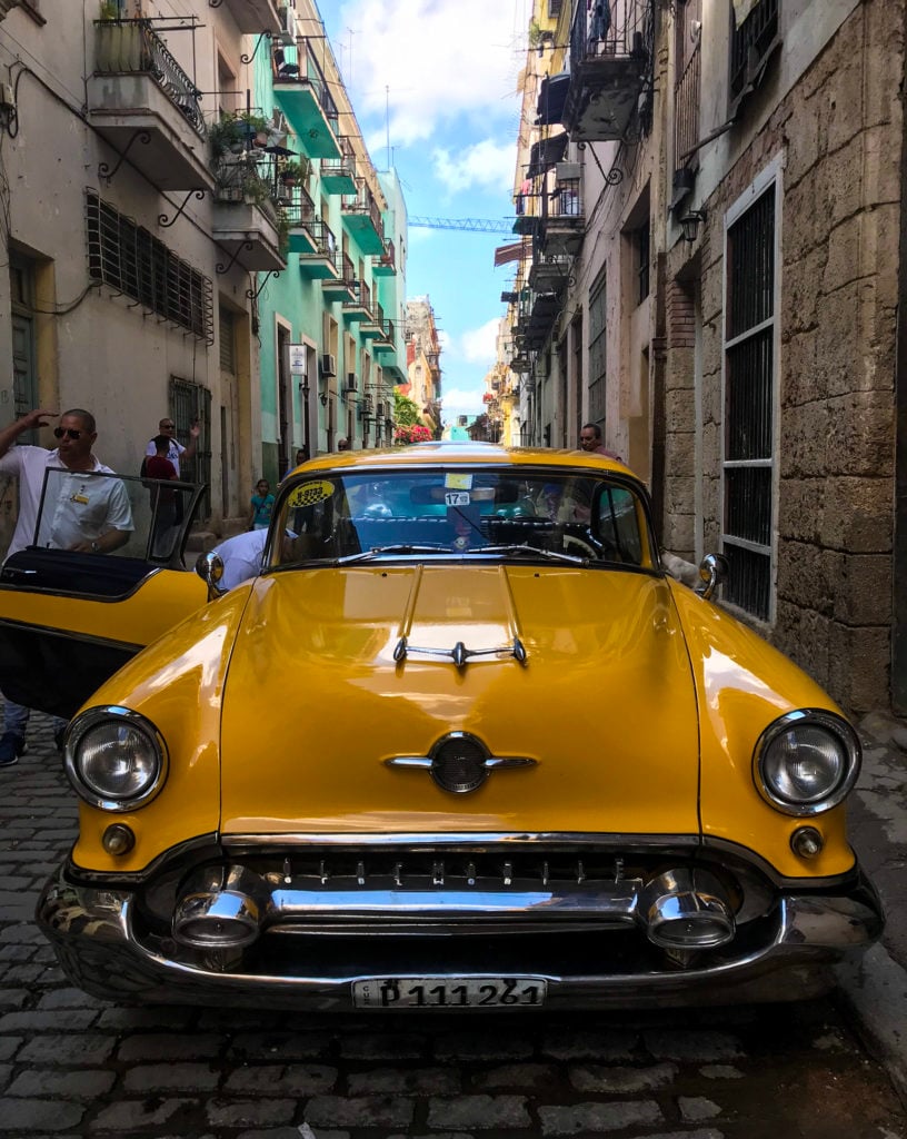 Havana Cuba small street with vintage yellow car in the foreground