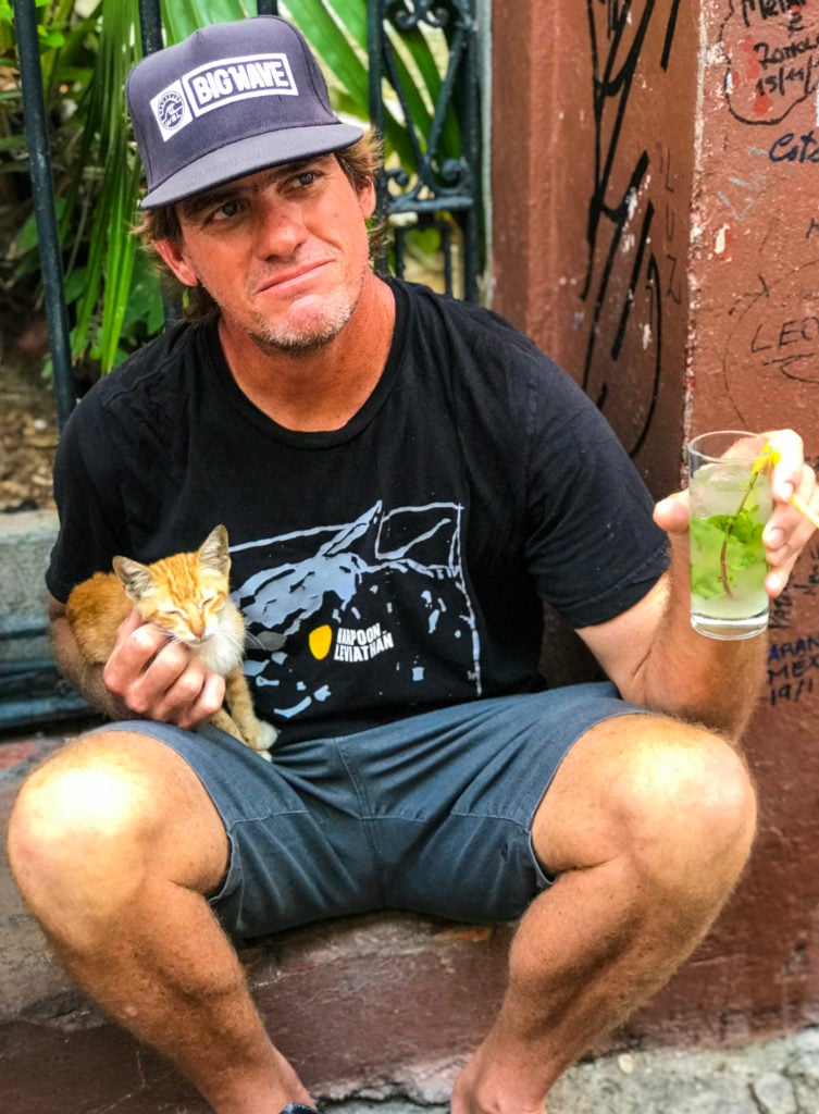 Man sitting in Havana Cuba drinking a mojito and petting a stray cat