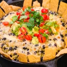 Chipotle Black Beans and Cilantro Rice Bake in a cast iron pan and topped with cheese, tomatoes, and avocados