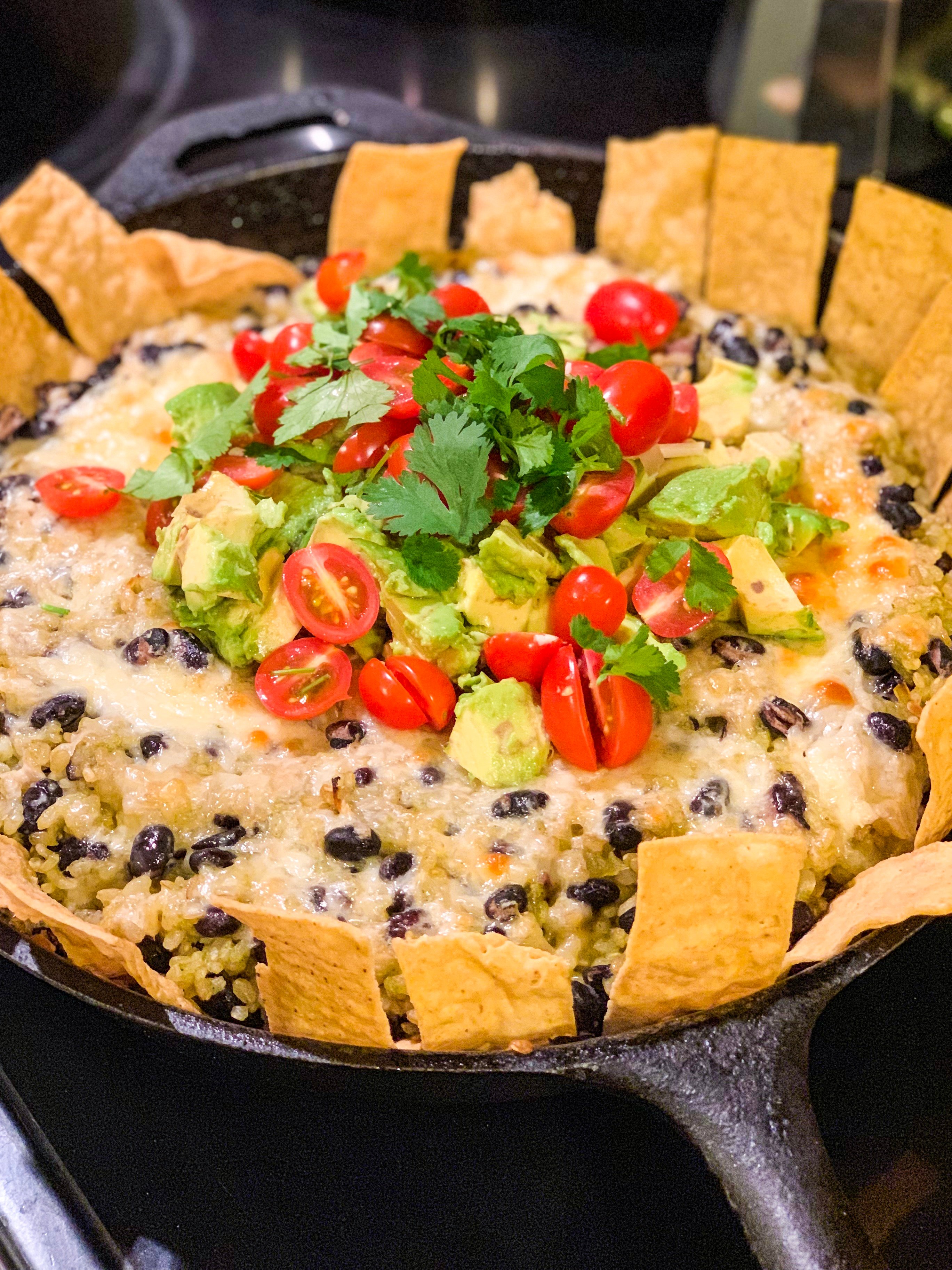 Chipotle Black Beans and Cilantro Rice Bake in a cast iron pan and topped with cheese, tomatoes, and avocados