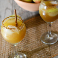 two wine glasses with apple cider mocktail with apples in the background