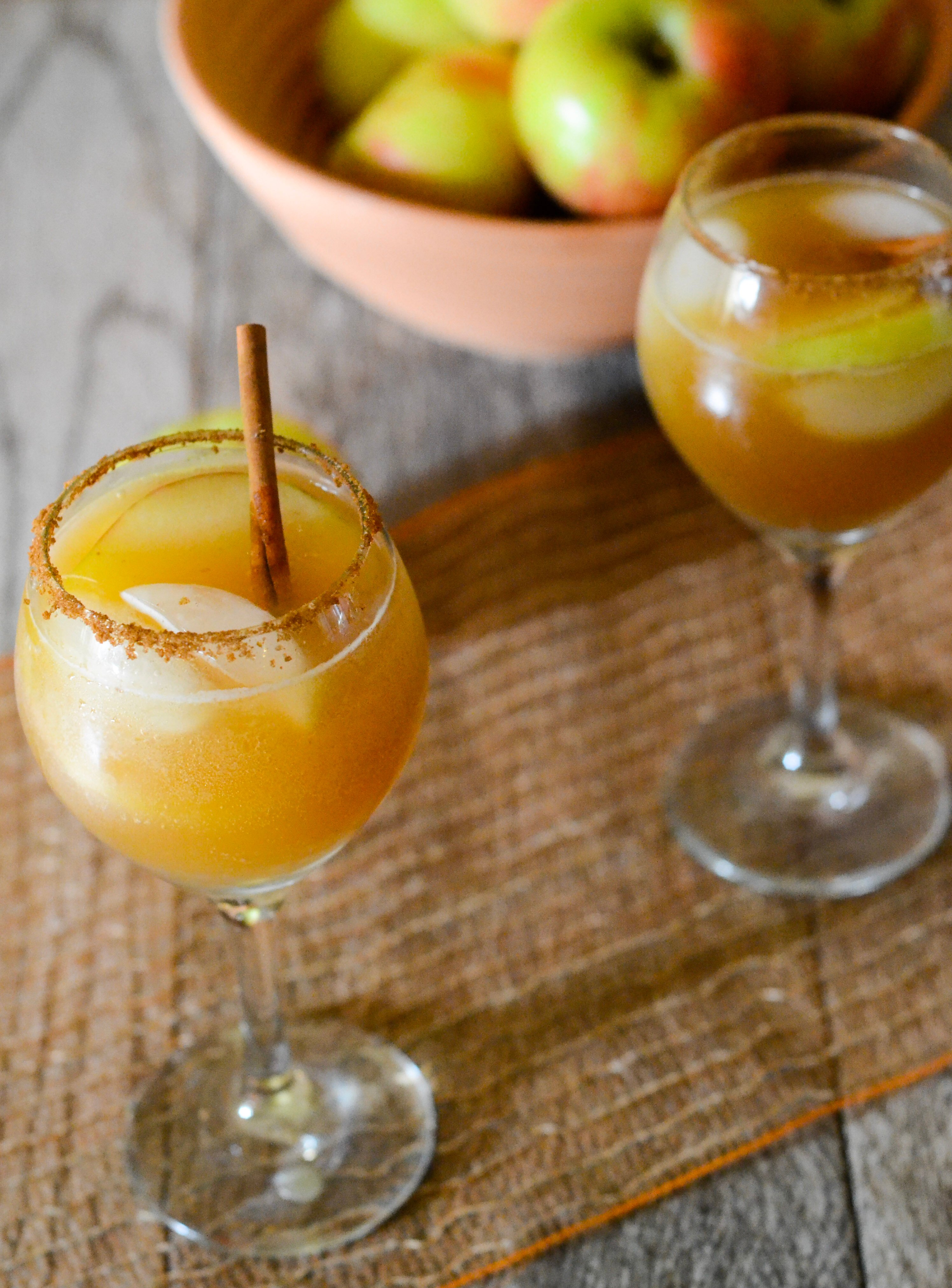 two wine glasses with apple cider mocktail with apples in the background