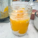 a smoothie with layers of coconut tapioca, mango and topped with sweetened condensed milk in the foreground, a dirty blender in the background